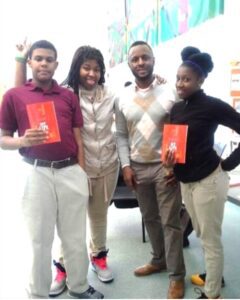 Four people holding up books in a room.