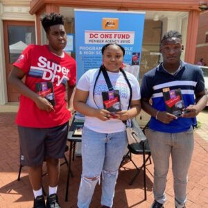 Three people holding up books outside of a building.